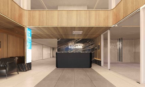 8.TSQ GF and Lounge An upscale, modern ground floor lobby and lounge at Triumph Square, with a black reception desk against a marbled wall, wood-paneled accents, and a comfortable black leather armchair.